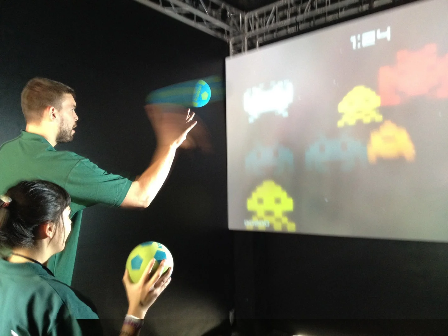 Two players throwing balls at a screen running the game.