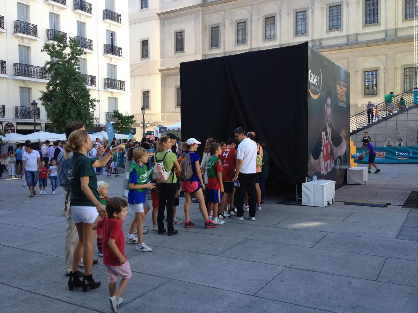 Kids and adults queuing at the promotional tent in a square.