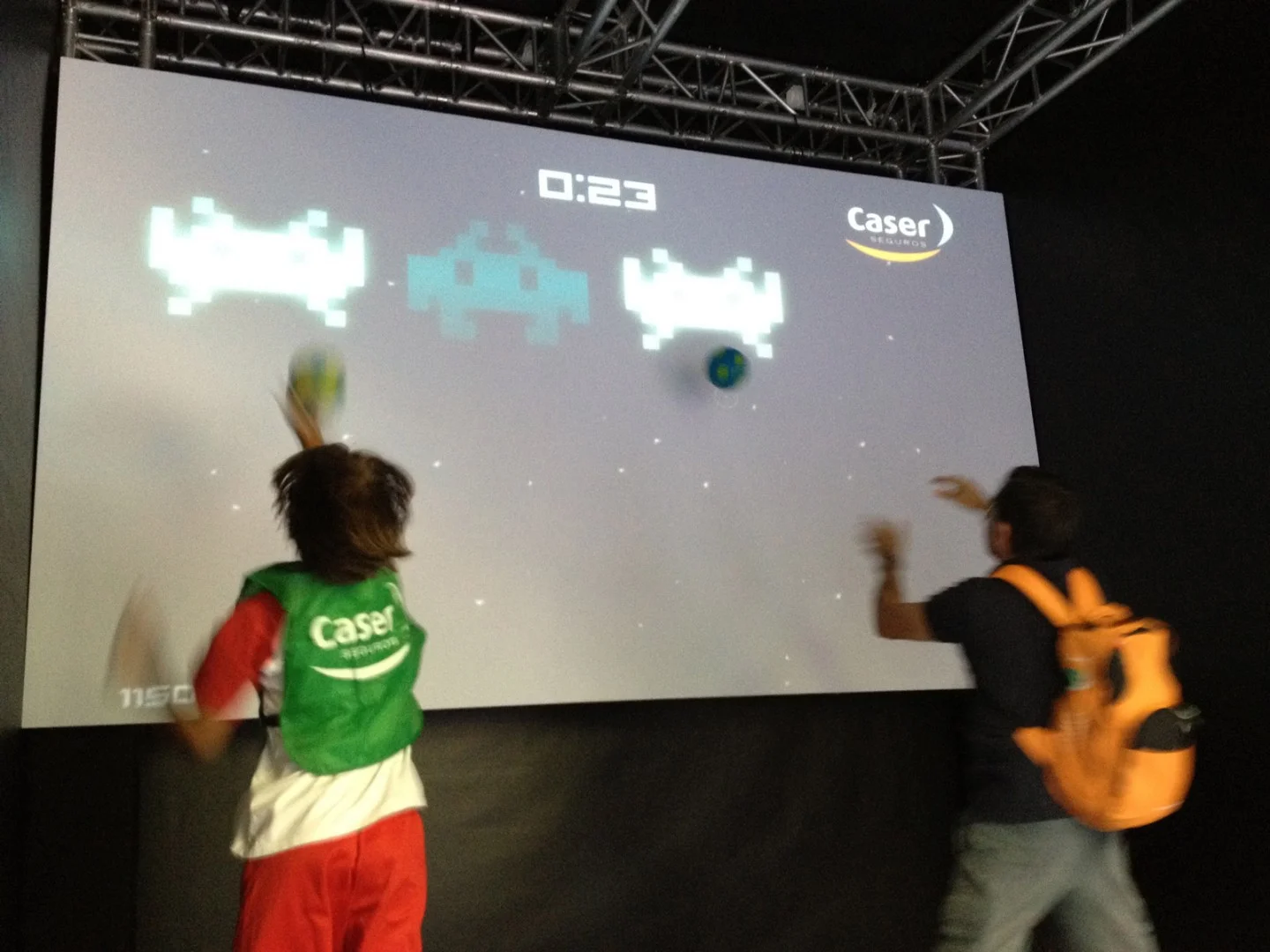 Two players throwing balls at a screen running the game.